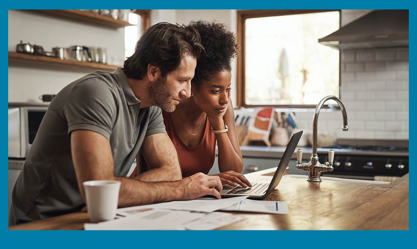 A mid 30s couple of mixed ethnic backgrounds working over a computer with documents out.